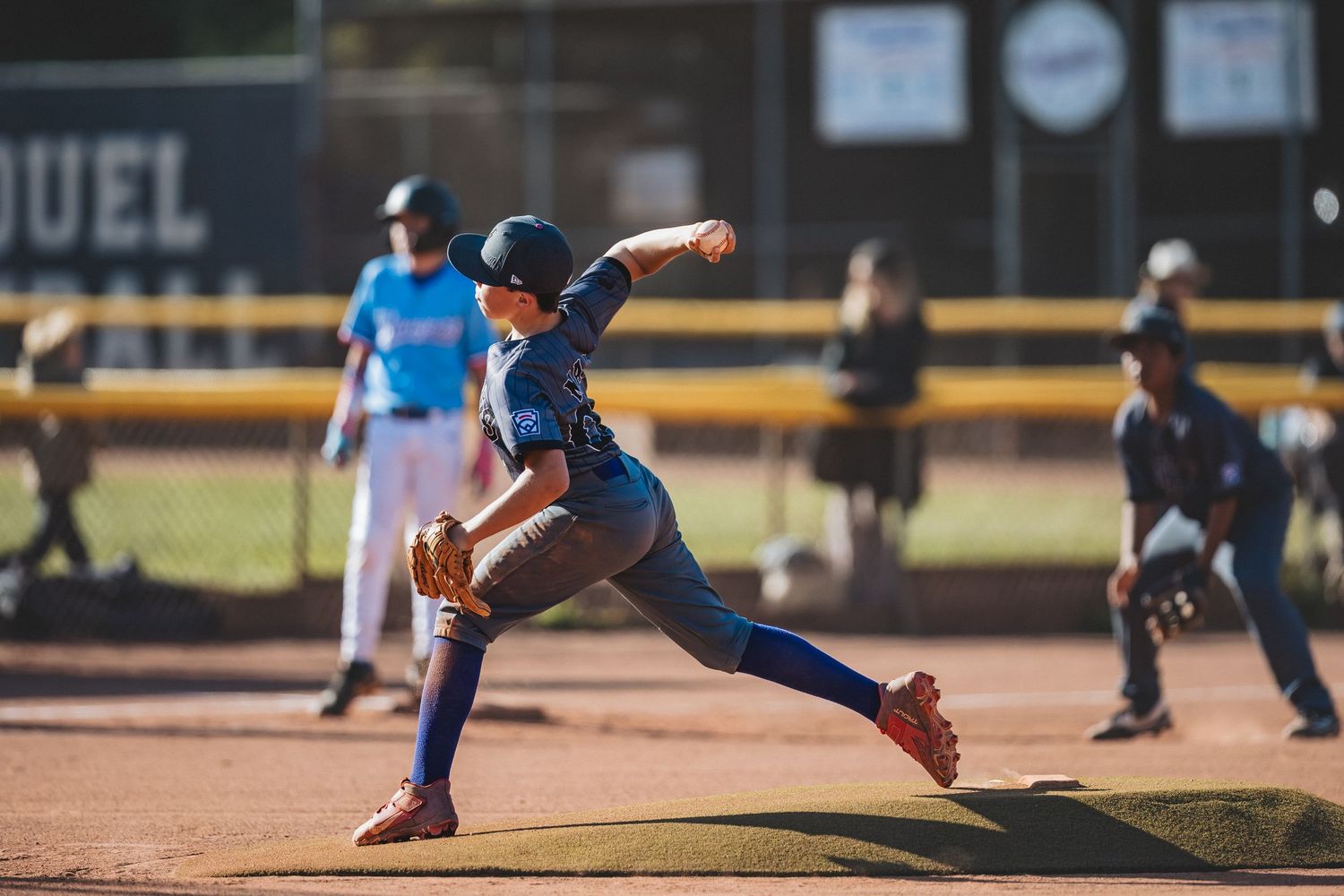 Baseball pitcher in blue uniform mid-delivery on dirt mound during daytime game.