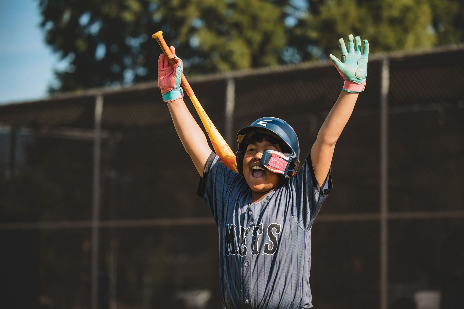 Baseball player raises arms in celebration wearing gray jersey and helmet on sunny field.