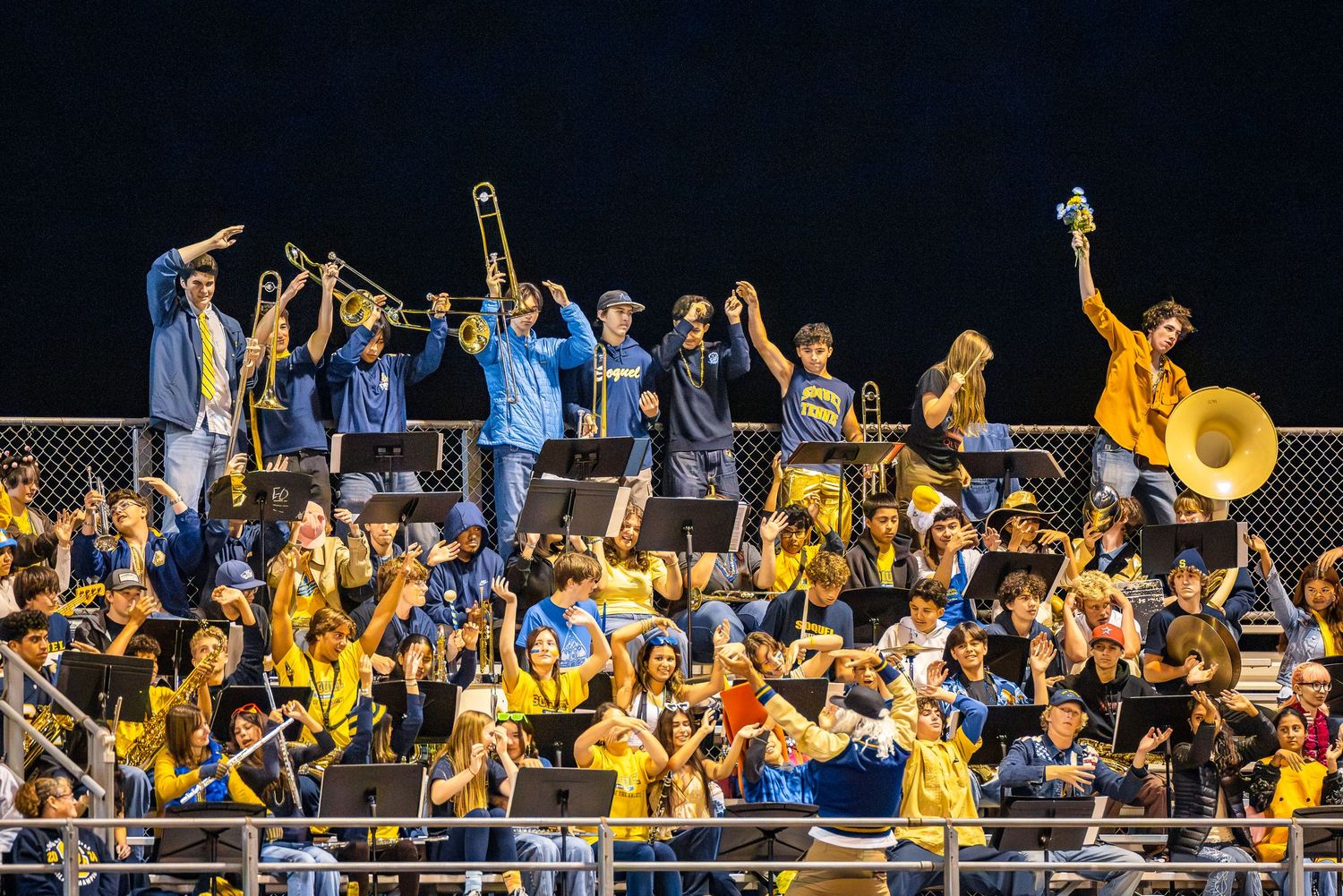 College marching band performs in bright yellow uniforms with enthusiasm during a football game performance.
