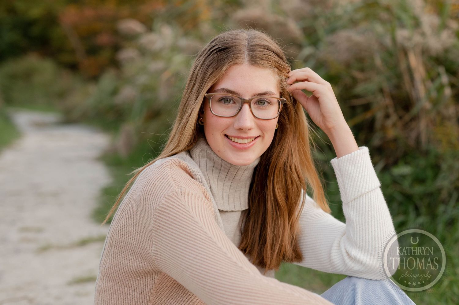 Portrait of someone in glasses and beige turtleneck sweater sitting outdoors in autumn setting.