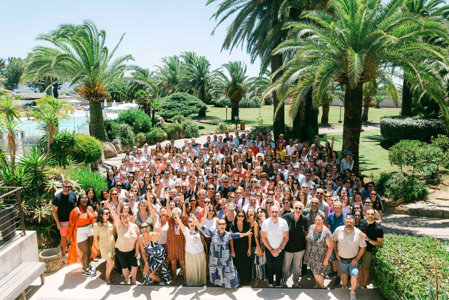 Large outdoor group gathering with palm trees and tropical landscaping at a resort venue during daytime.