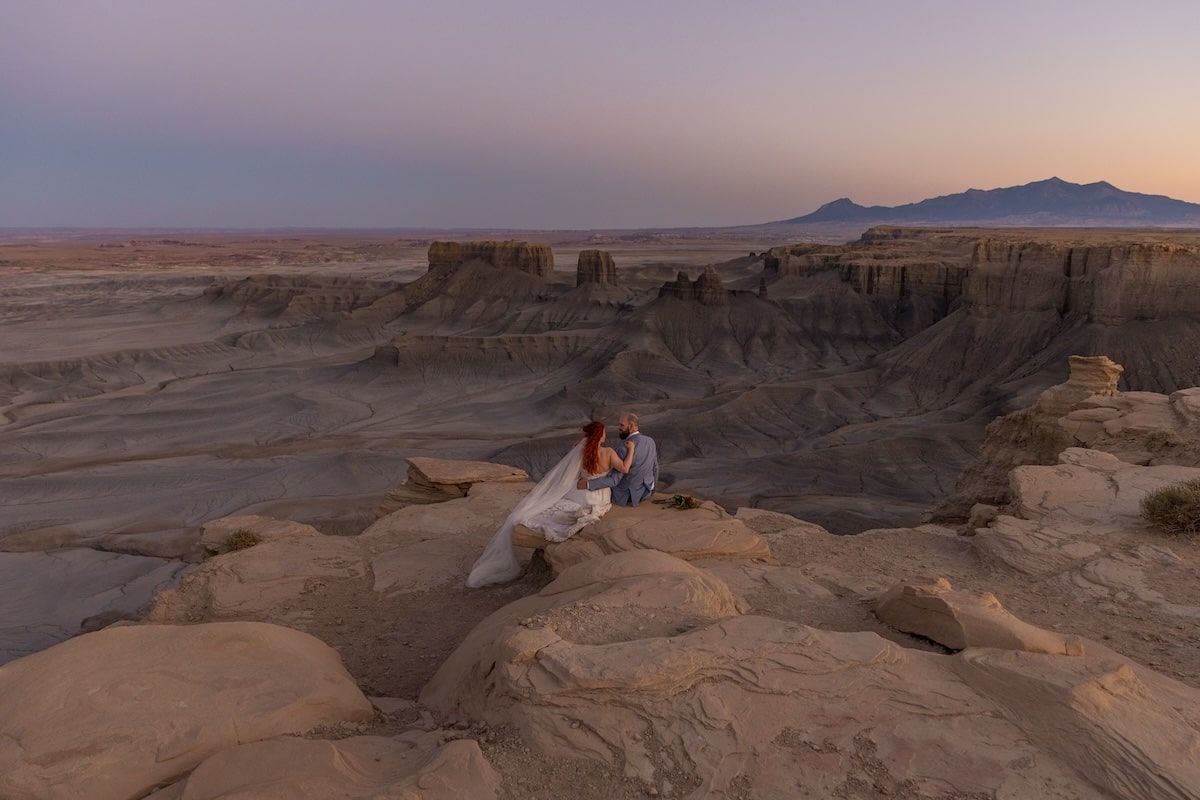 People watching sunset over red rock formations in Moab Utah against an orange and purple desert sky.