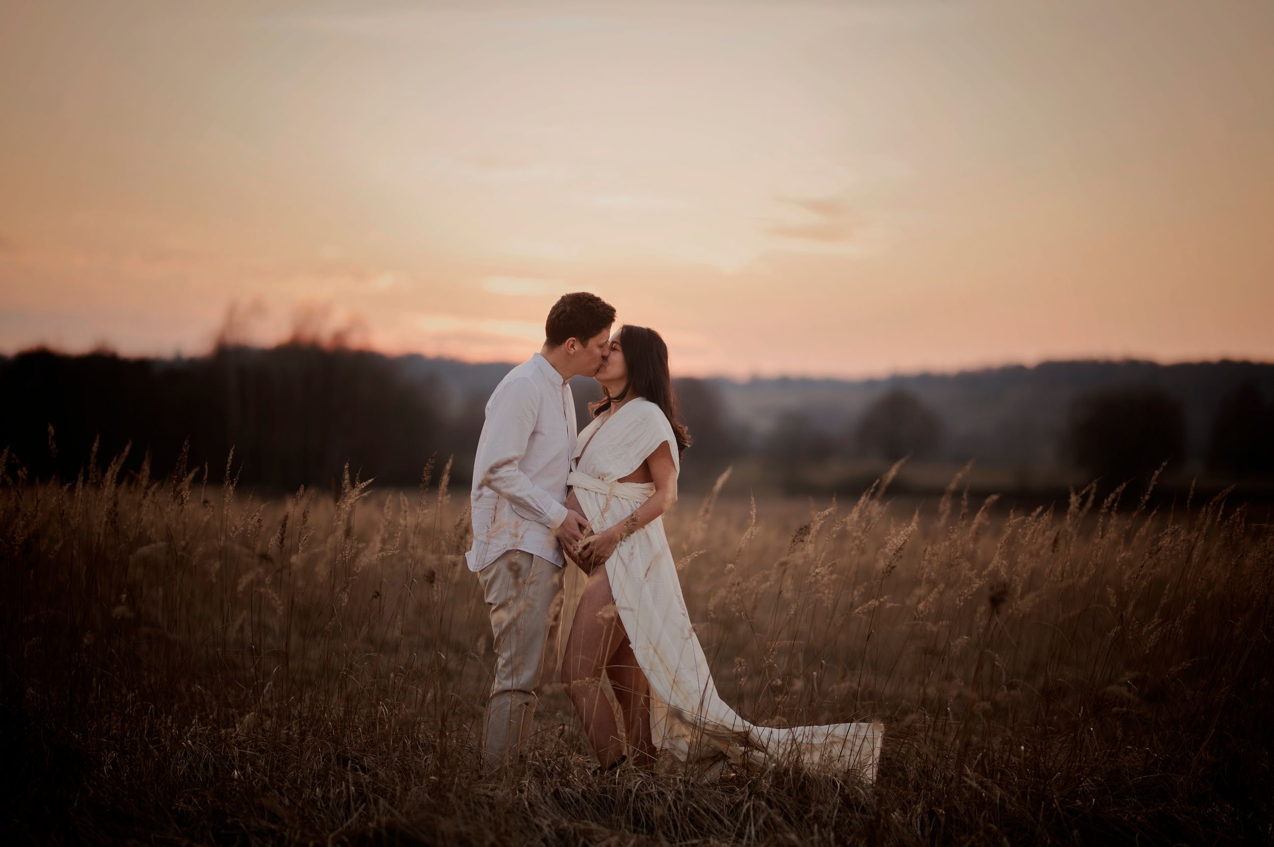 A romantic couple embraces in a golden field at sunset during their engagement photography session.