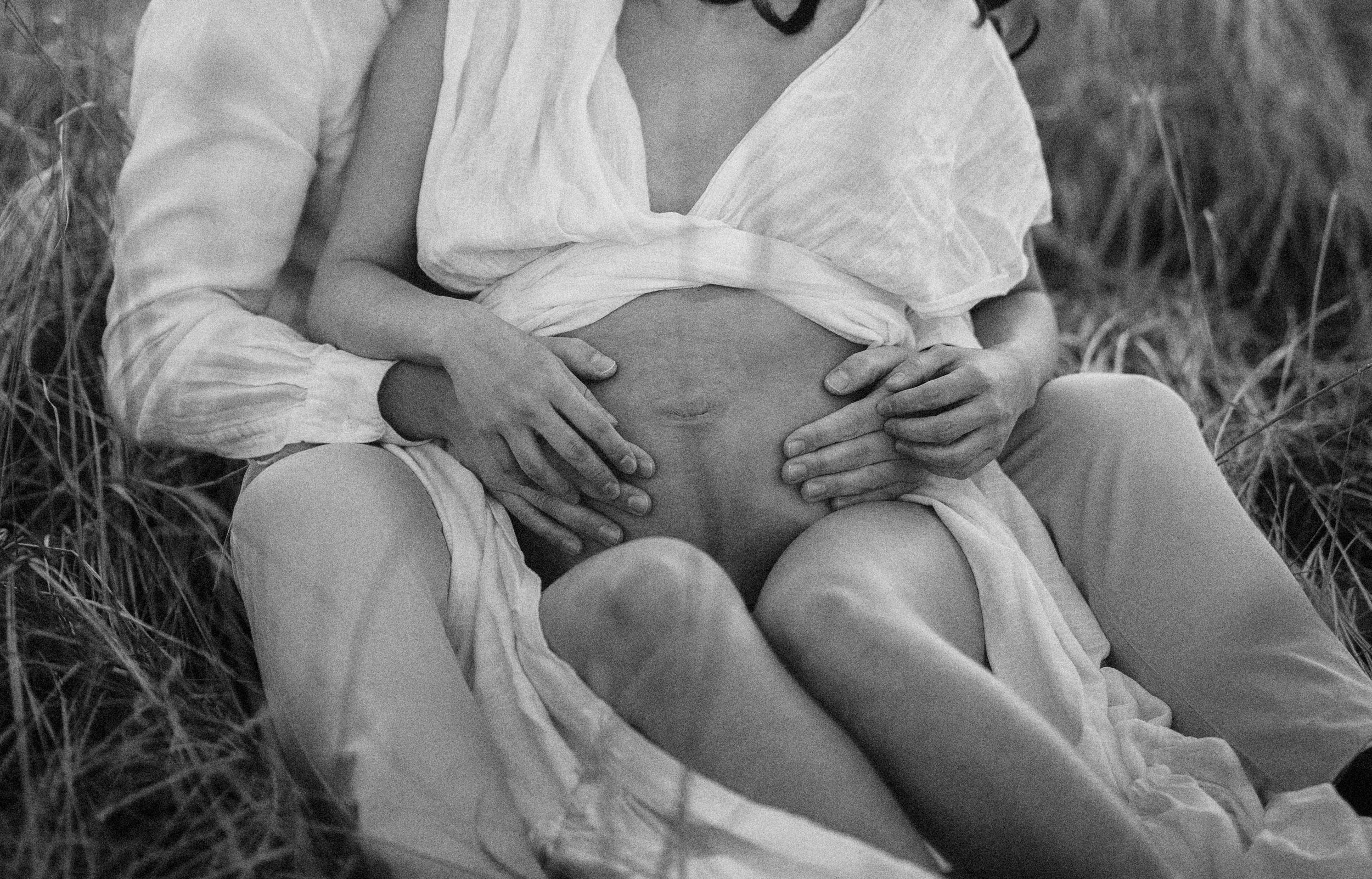 Black and white close up photograph showing an intimate moment between a couple sitting in tall grass.