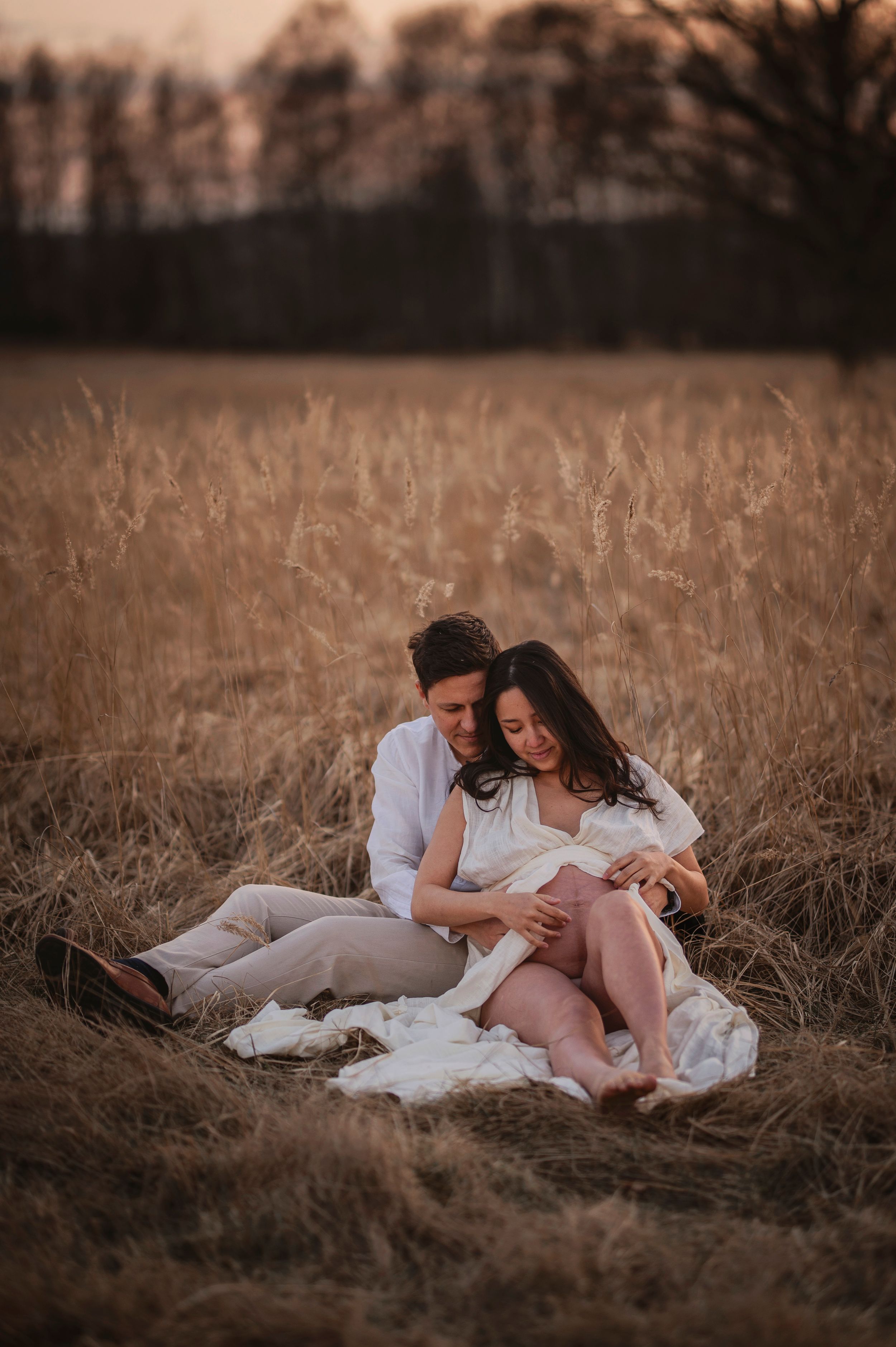 A couple sits in a golden wheat field at sunset sharing an intimate moment together.
