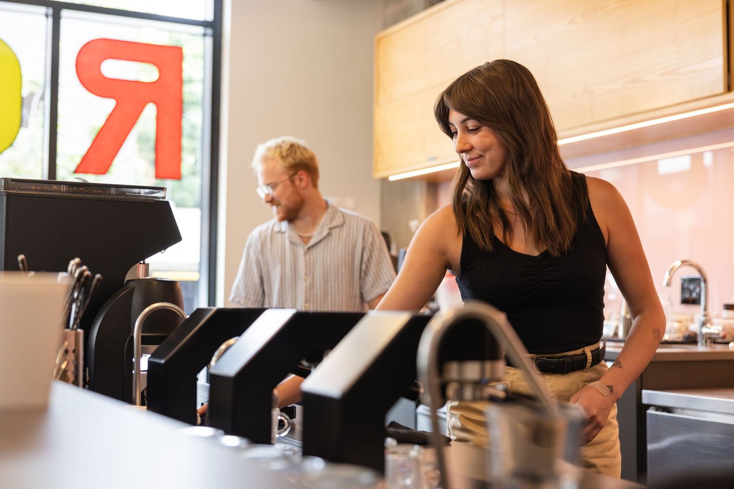 Baristas working behind counter at modern coffee shop with equipment and minimalist decor.