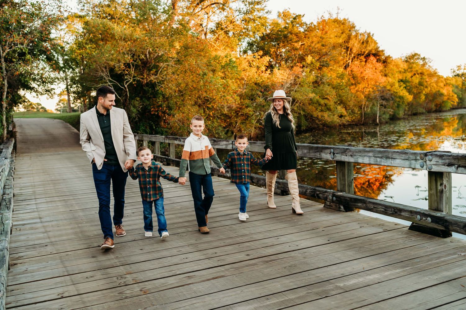 Family walking together on wooden boardwalk during autumn with golden trees reflecting in water. Family Portraits in Alexandria, La