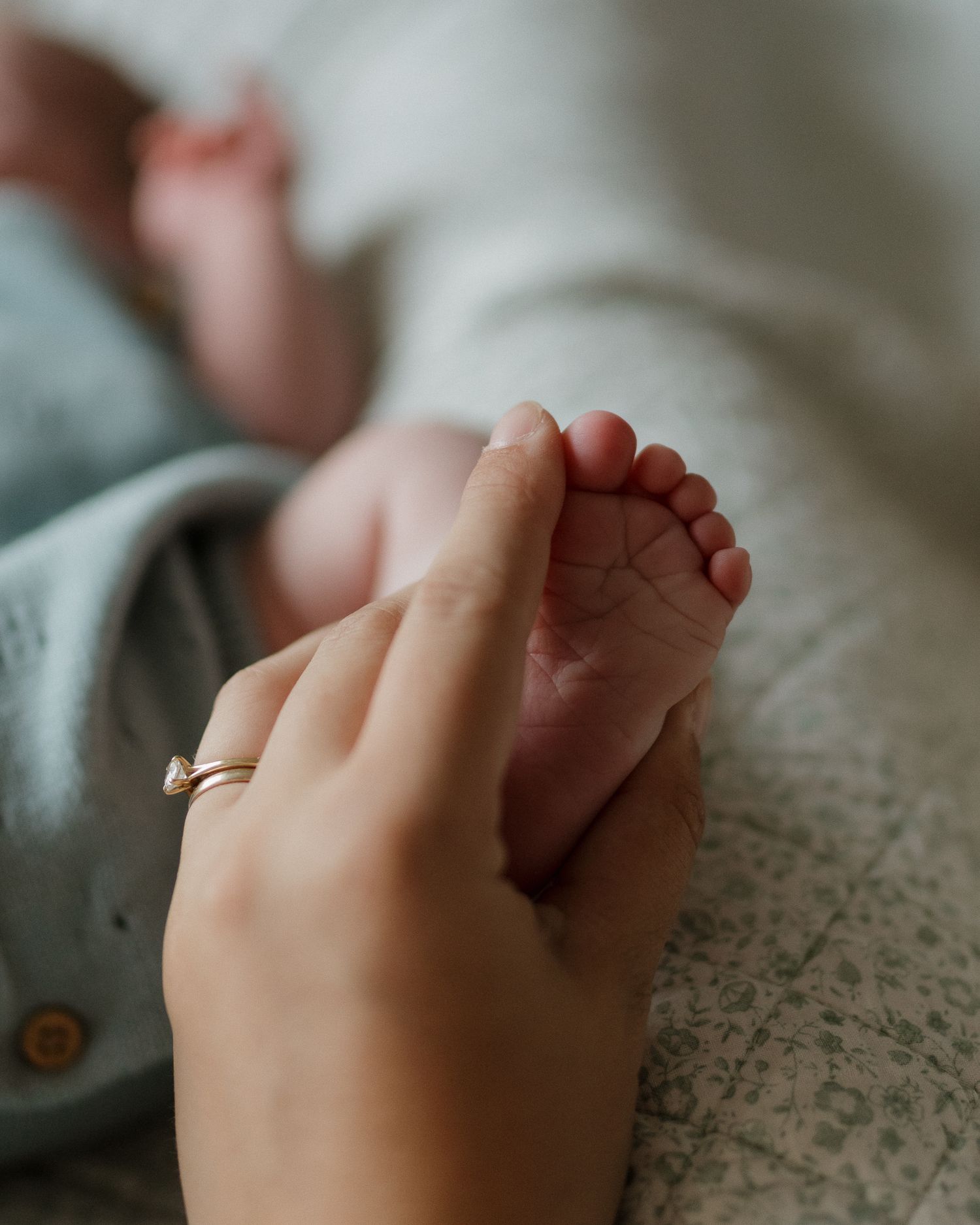 A tiny baby's foot being gently held by an adult hand wearing a wedding ring.