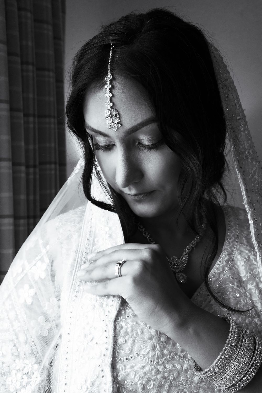 Black and white portrait of a bride in traditional Indian bridal attire with maang tikka jewelry and embroidered dupatta.