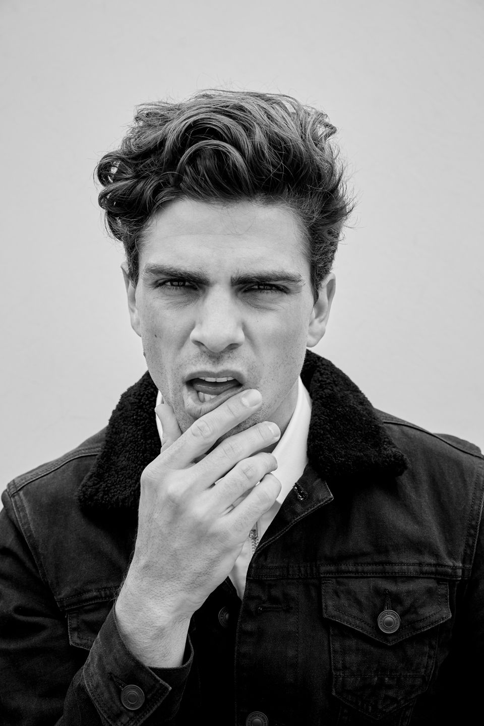 Black and white portrait of a person in denim jacket with thoughtful expression touching their face.