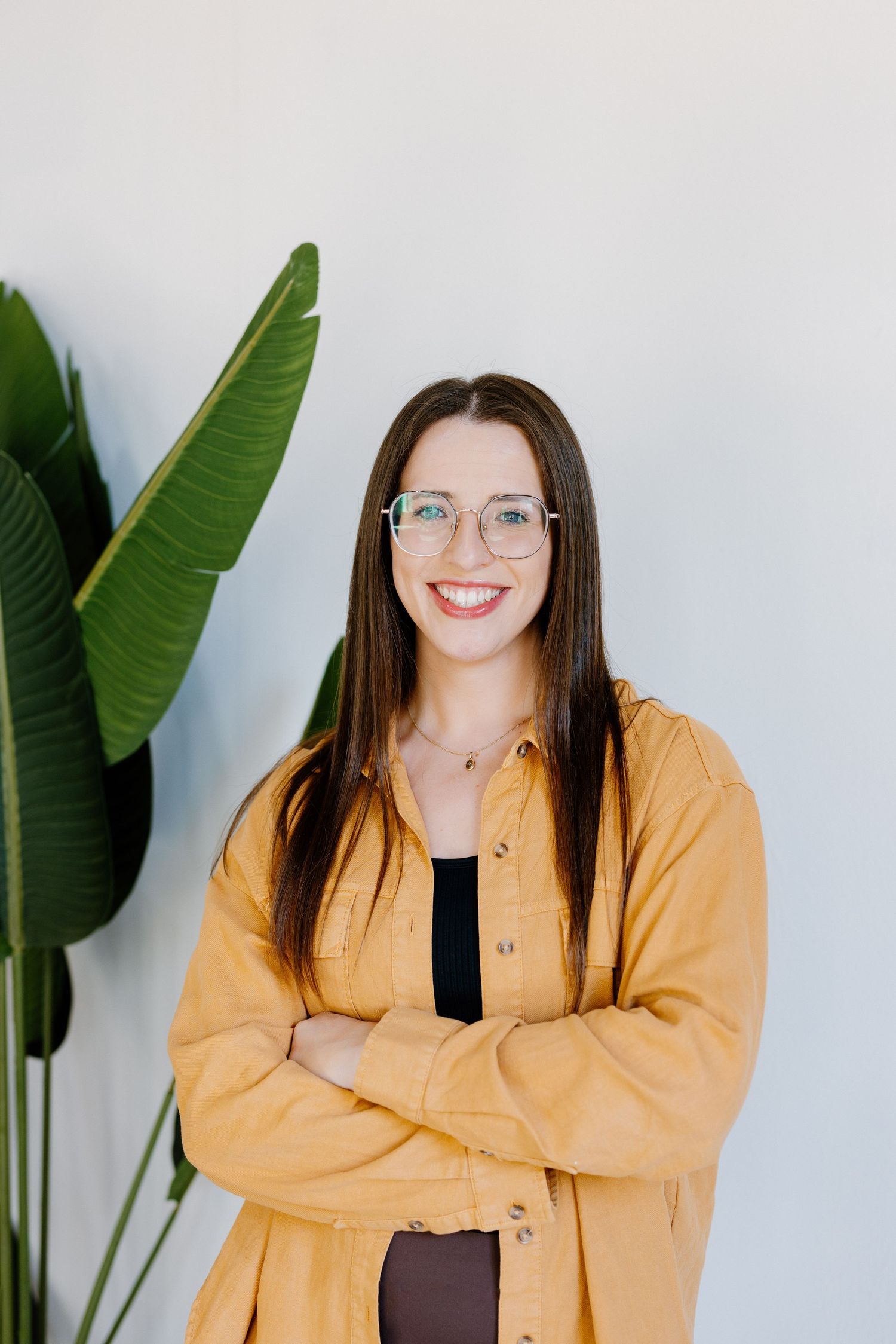 Person in yellow cardigan poses by tropical plant against white wall.