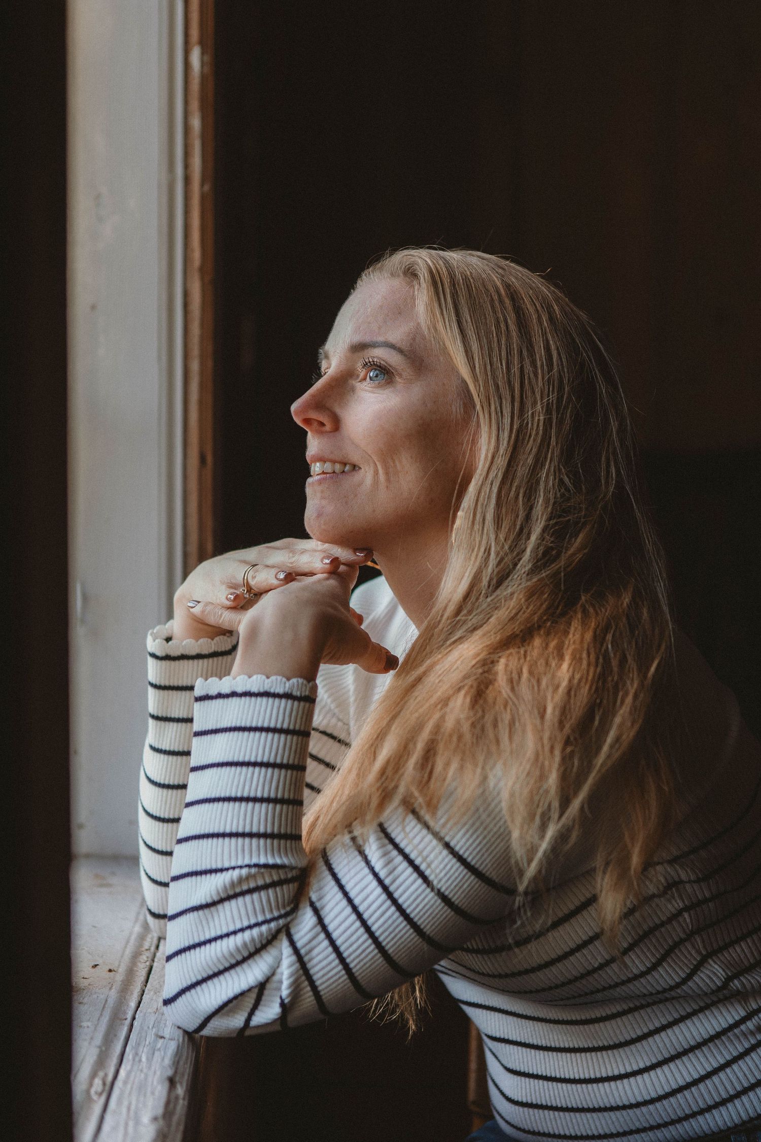 Person in striped sweater gazing thoughtfully out window in profile.