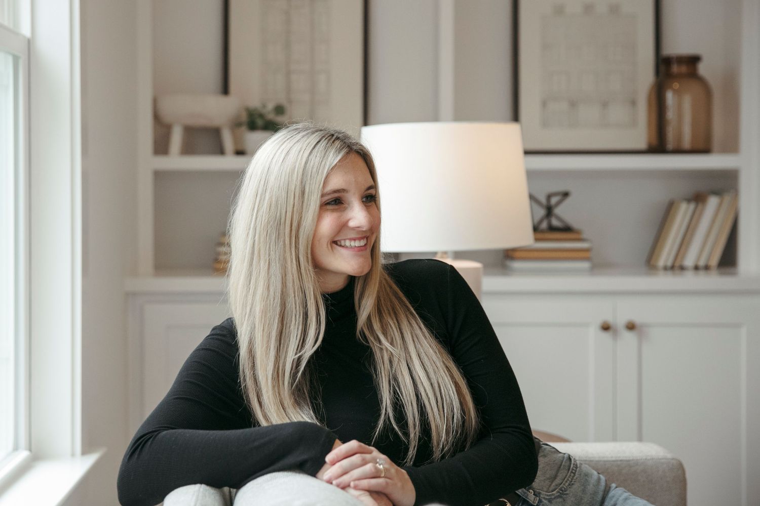 A cozy indoor portrait showing someone relaxing on a sofa beside built-in shelving and a table lamp.
