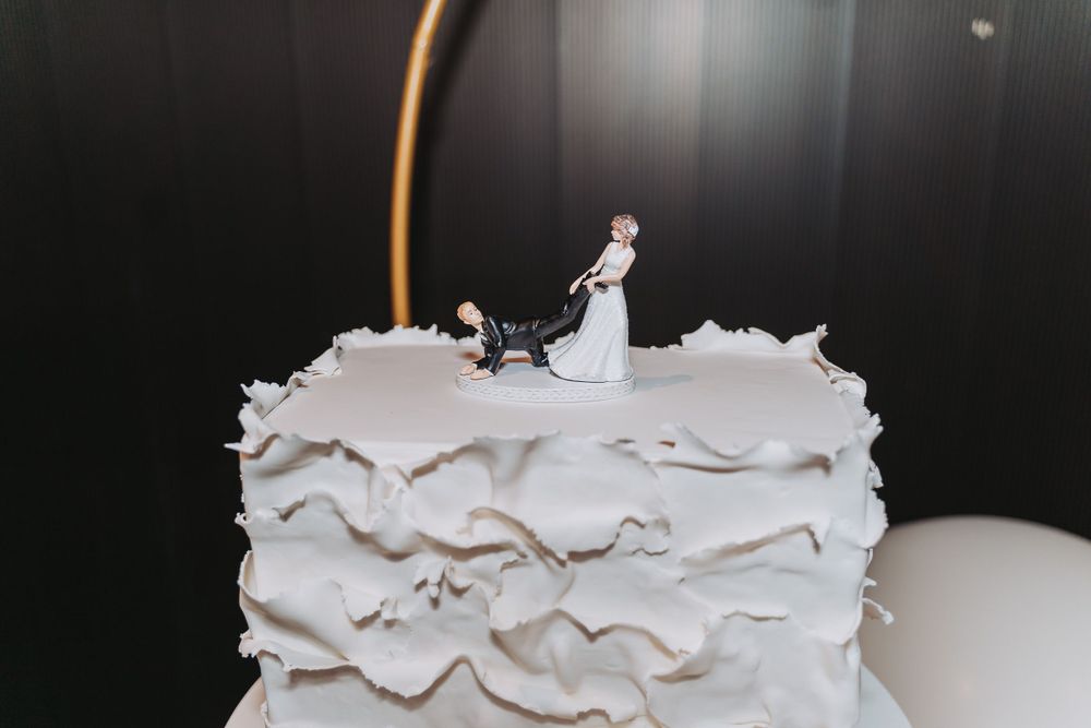 Close-up view of a textured white wedding cake with traditional bride and groom figurine topper.