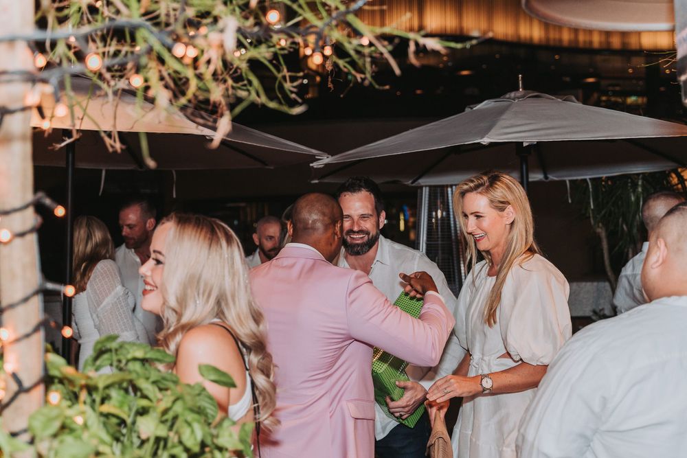 A group of elegantly dressed guests enjoying conversation under outdoor umbrellas at a social gathering.