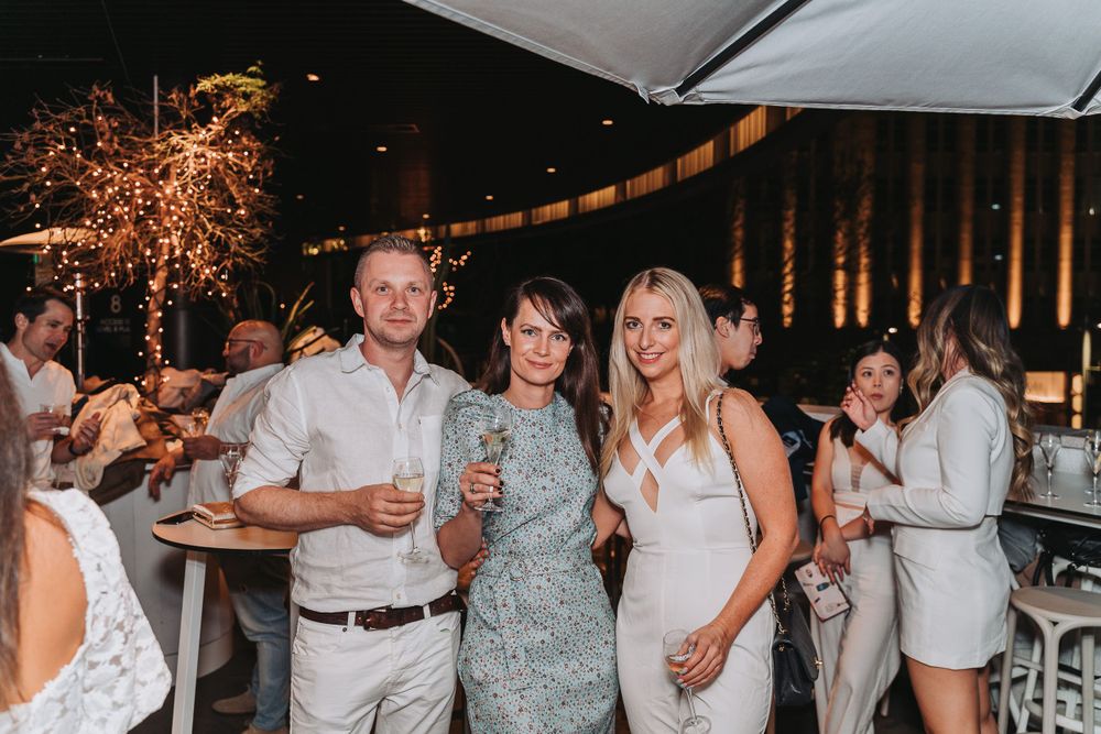 Wedding guests enjoy themselves at an outdoor evening reception with festive string lights and a bar area.