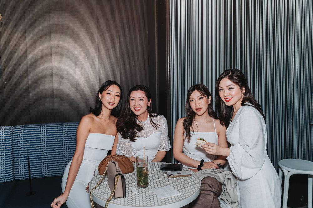 Four friends enjoying drinks and conversation together at a restaurant table with modern decor and blue seating.