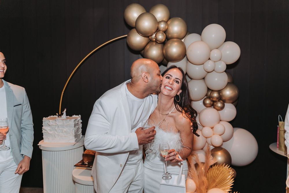 Wedding reception celebration at night with elegant balloon arch and wedding cake in white and gold decor.
