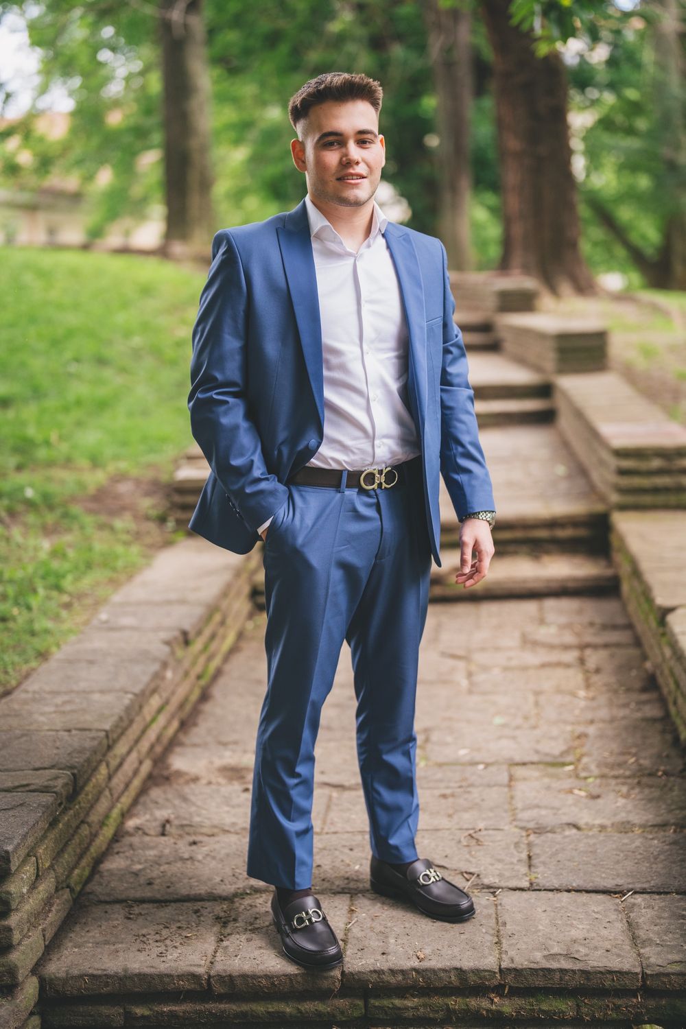 Person wearing a blue suit posing on stone steps outdoors.