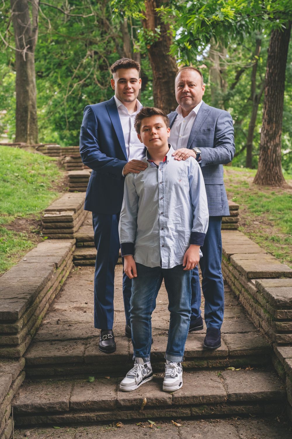 Three people in formal attire standing together on stone steps outdoors.