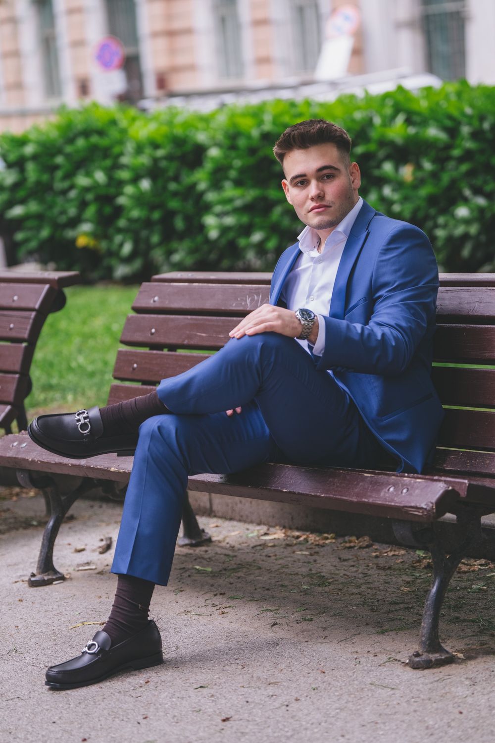 A person in a blue suit sits confidently on a wooden park bench.