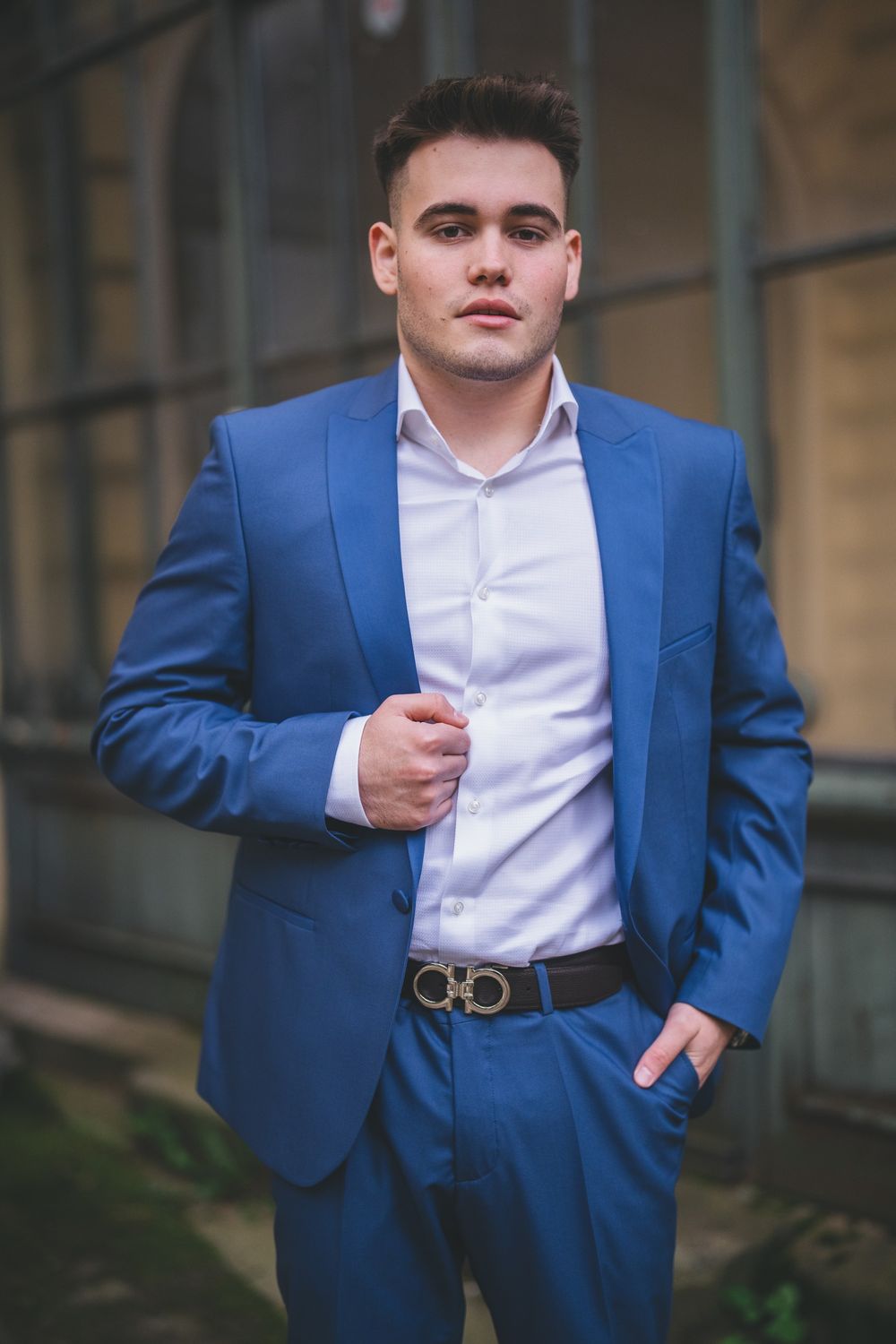 A person in a crisp blue suit and white shirt poses against a stone building exterior.