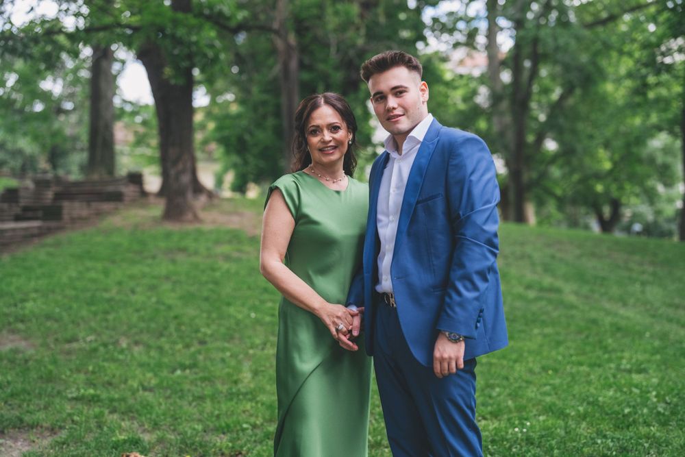 A pair pose together outdoors, one in a green dress and one in a blue suit.