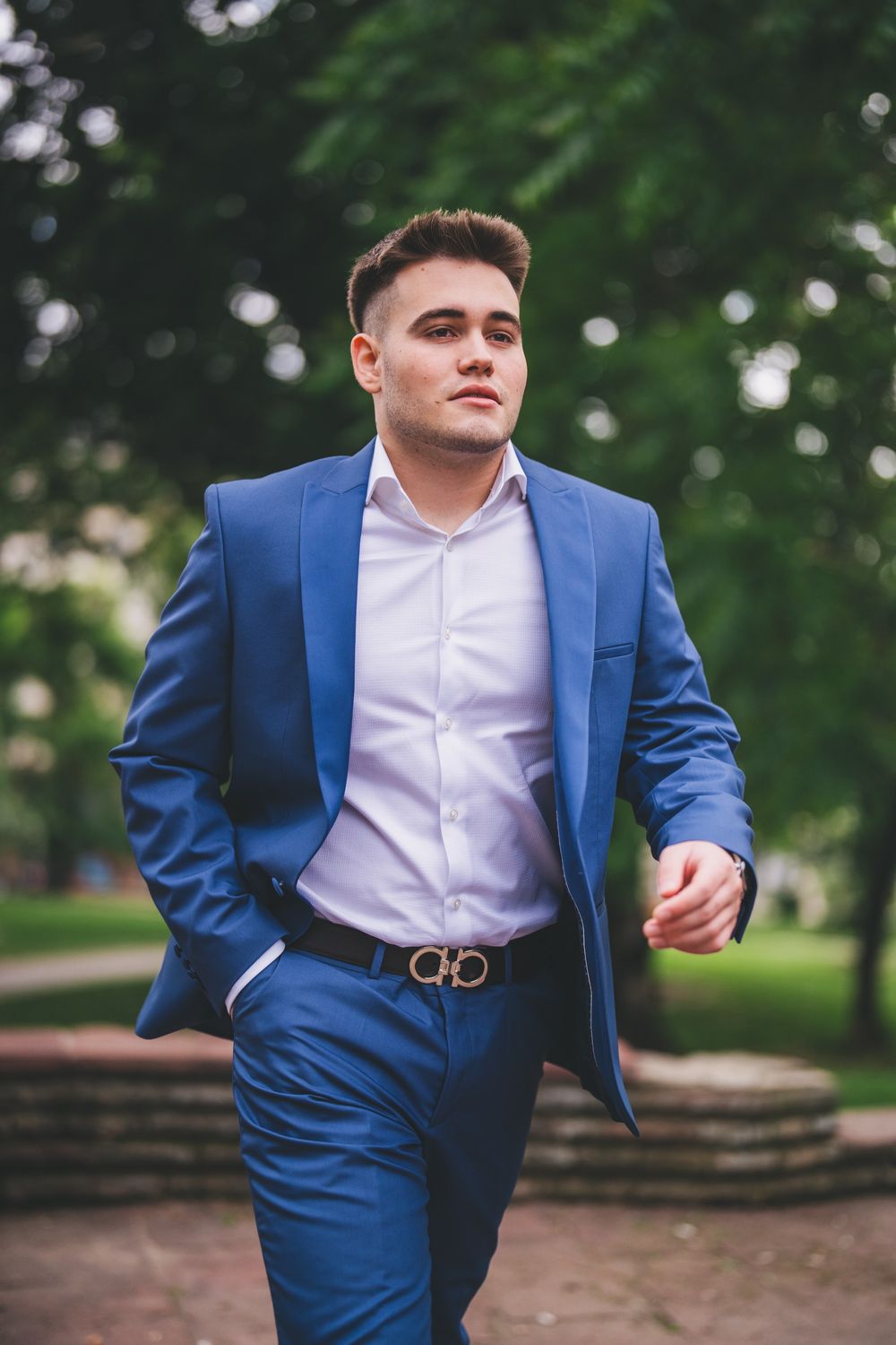 Professional in a tailored blue suit walks confidently through an outdoor garden setting.