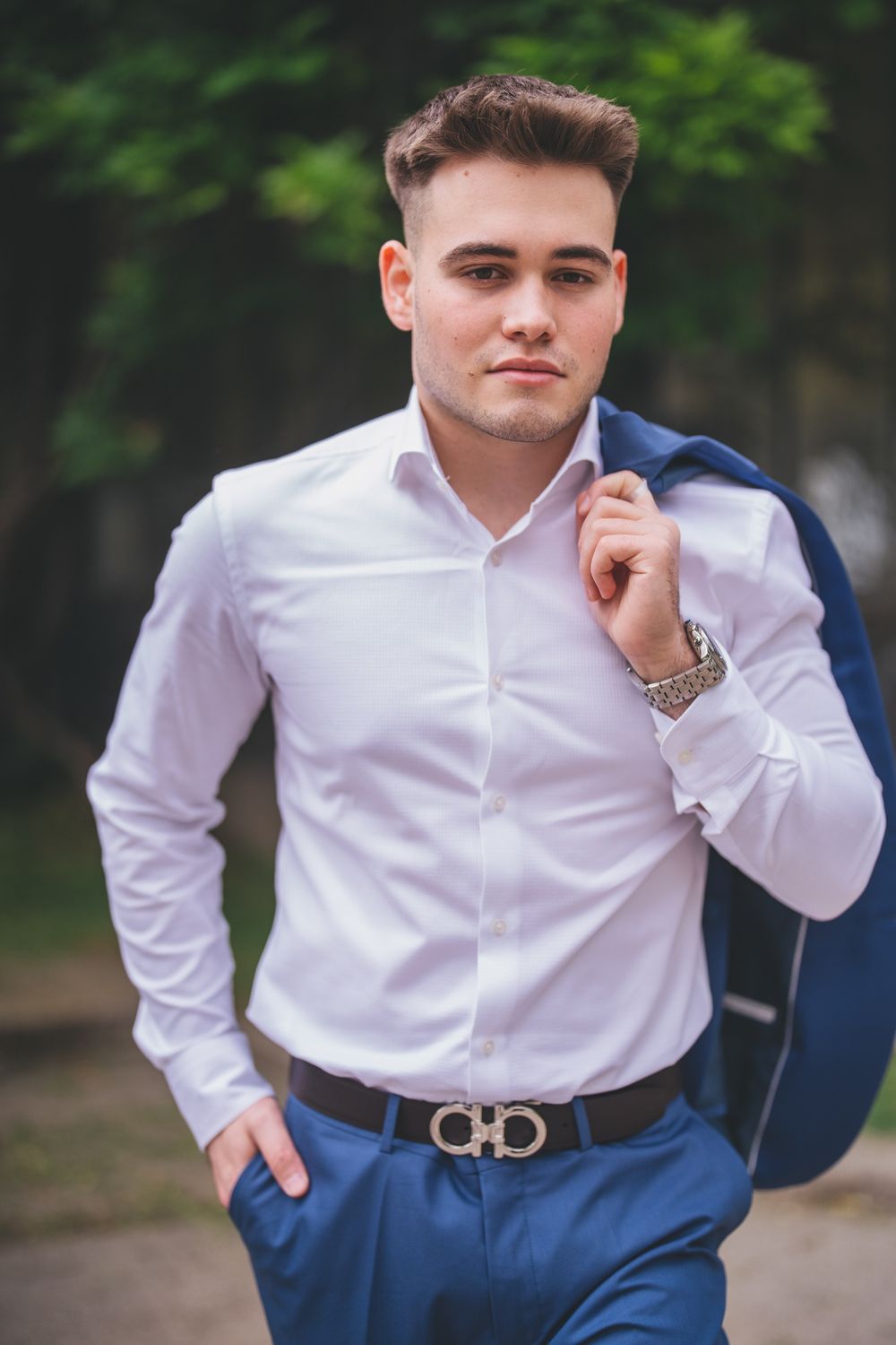 Professional headshot of someone wearing a crisp white shirt and blue blazer against a blurred natural background.