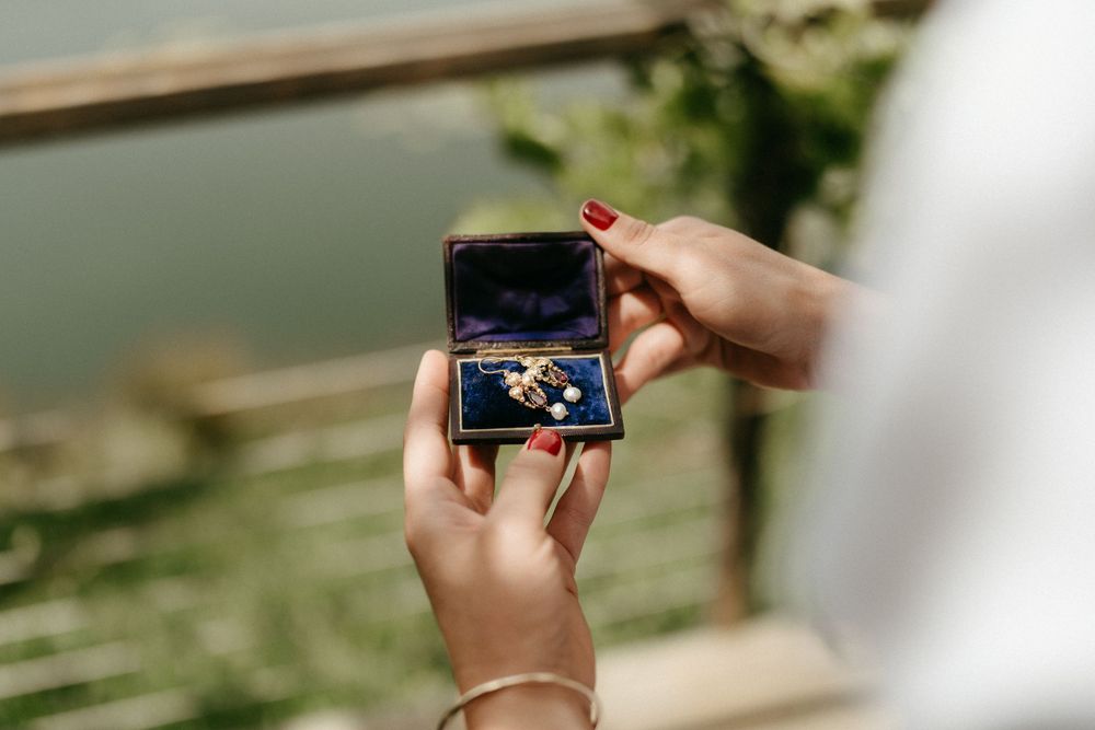 Hands holding open a small jewelry box during an outdoor wedding moment.