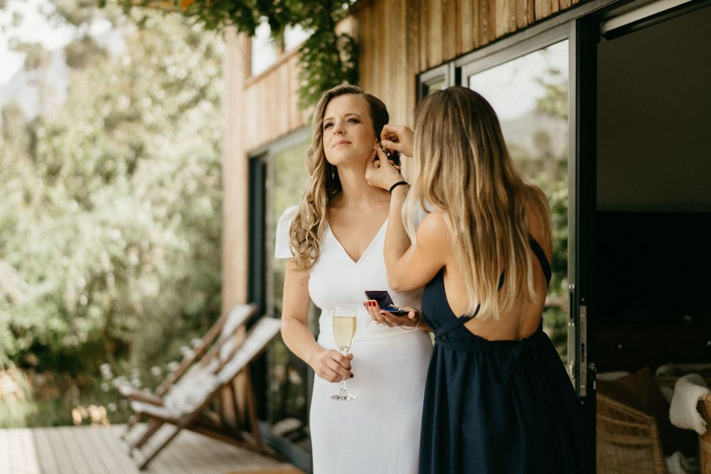 Wedding preparations outdoors as a woman in white gets ready with help from another in navy.
