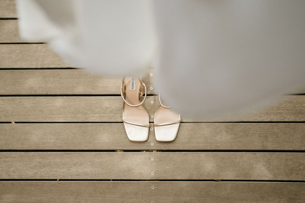 White bridal sandals positioned on wooden deck with flowing fabric.