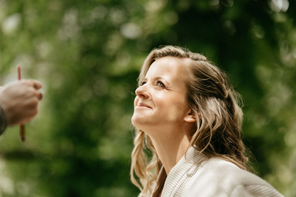 A person looking up with a joyful expression while standing outdoors with sunlit trees in the background.