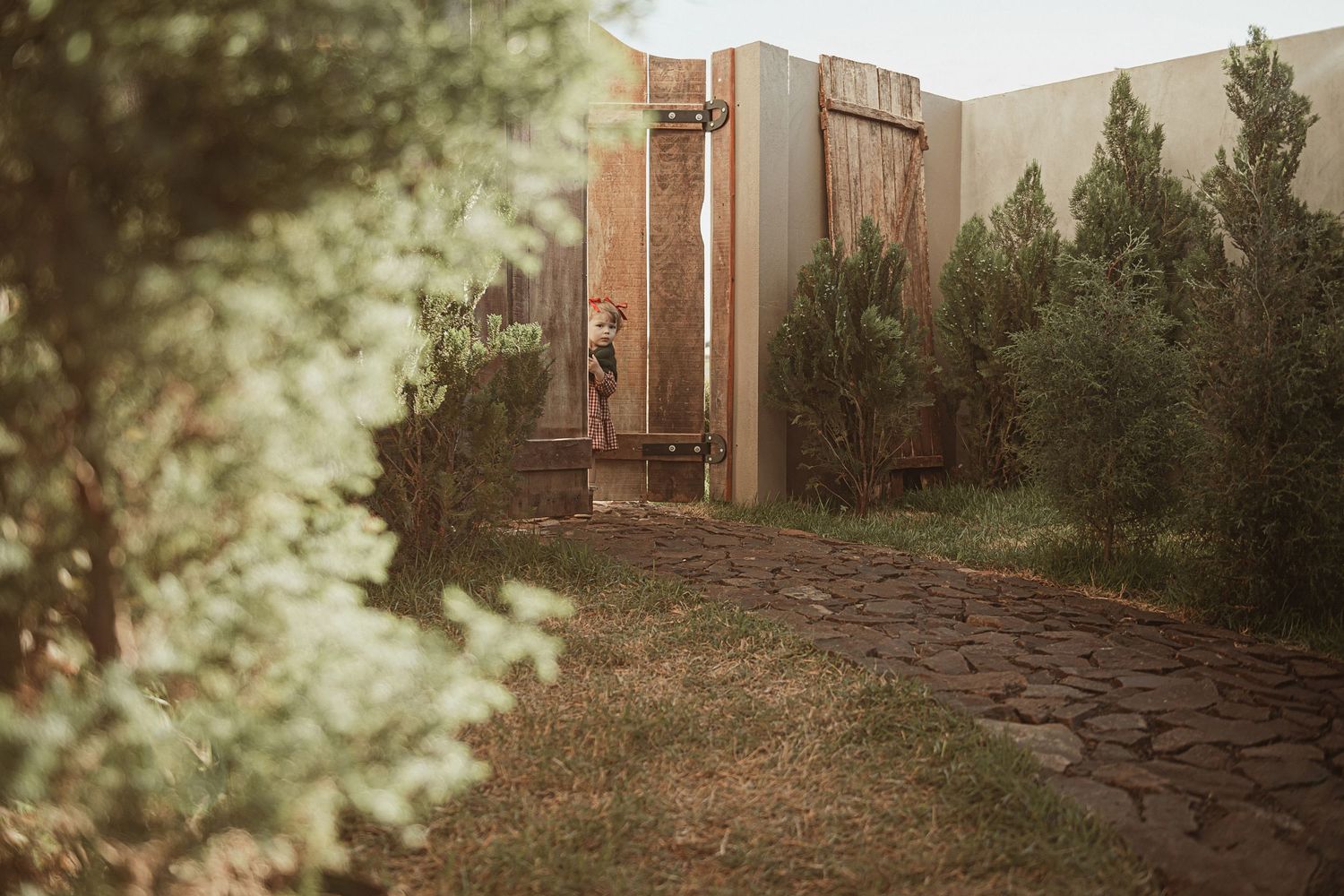 A rustic stone pathway leads to a wooden door surrounded by evergreen trees in a peaceful outdoor setting.