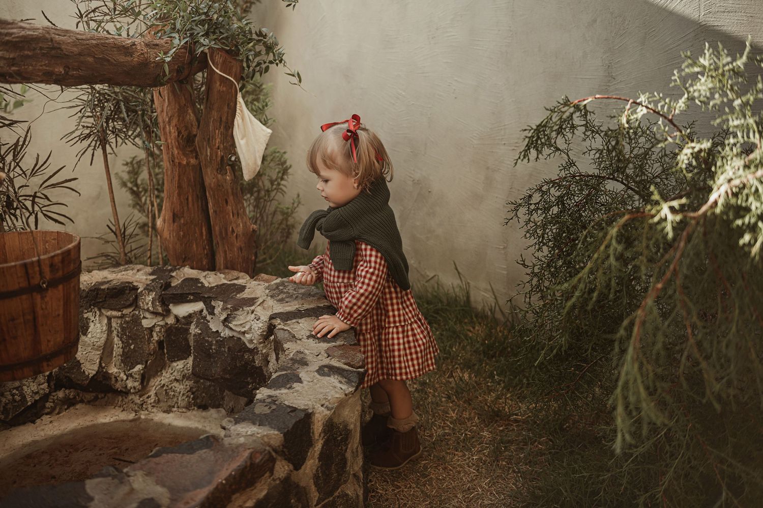 A small figure in a gingham dress explores a whimsical garden pathway with stone steps and lush greenery.