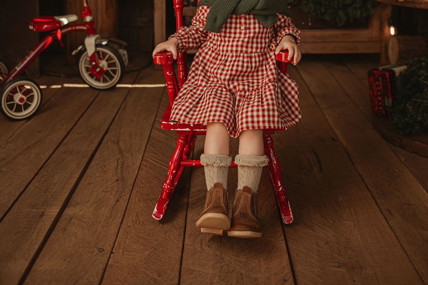 Red and white gingham dress and cozy boots sitting on wooden floors next to a vintage tricycle.