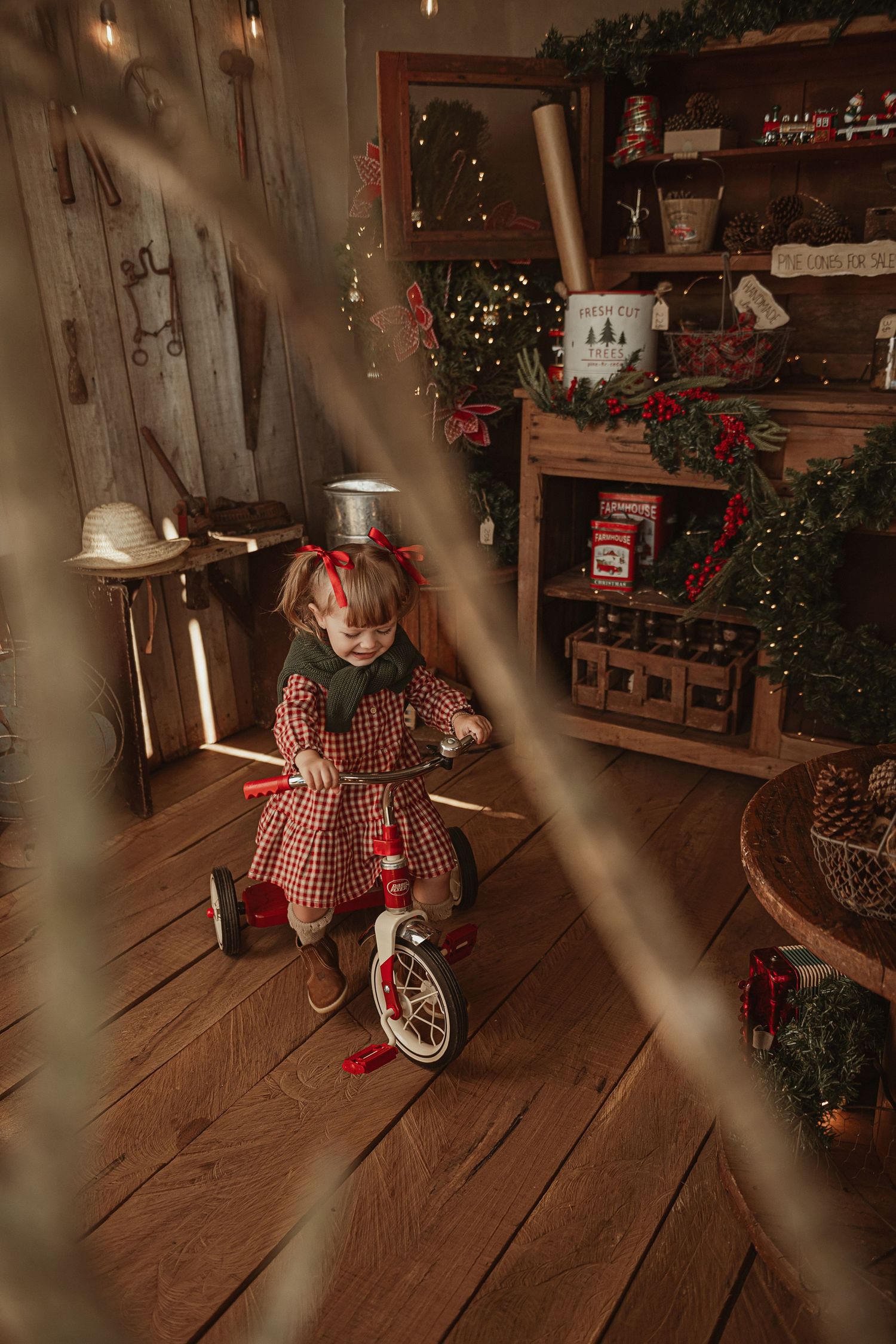 Festive holiday scene with red tricycle, wooden shelves, and Christmas decorations in a warm rustic room.