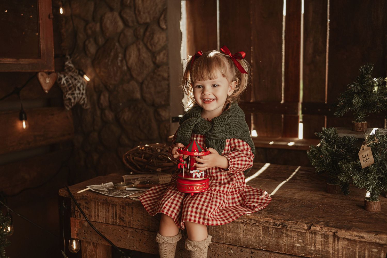A cozy Christmas scene with a child in gingham dress sitting on rustic wooden furniture amid holiday decorations.