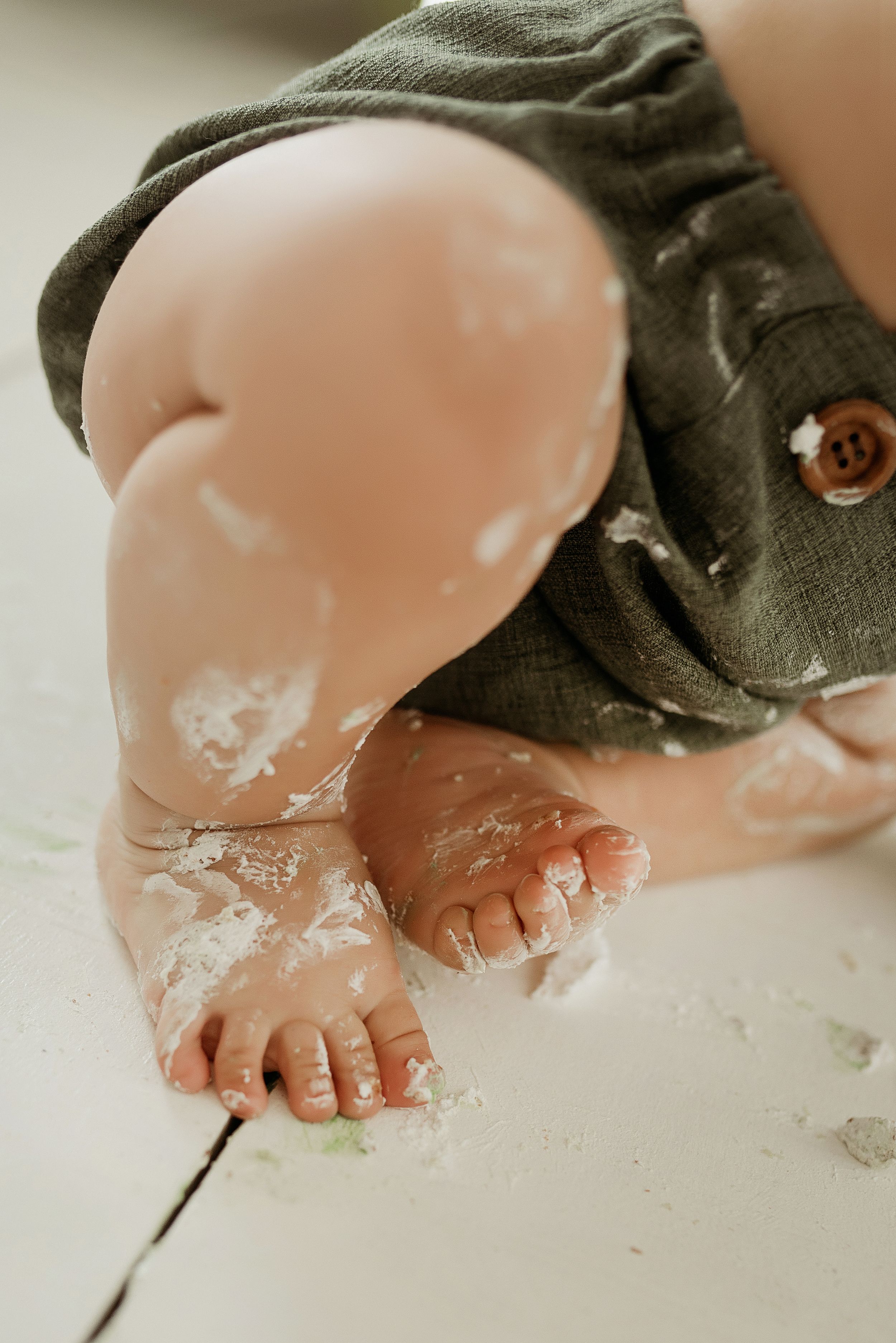 Small bare feet covered in white flour or powder on a light colored surface with green fabric visible.