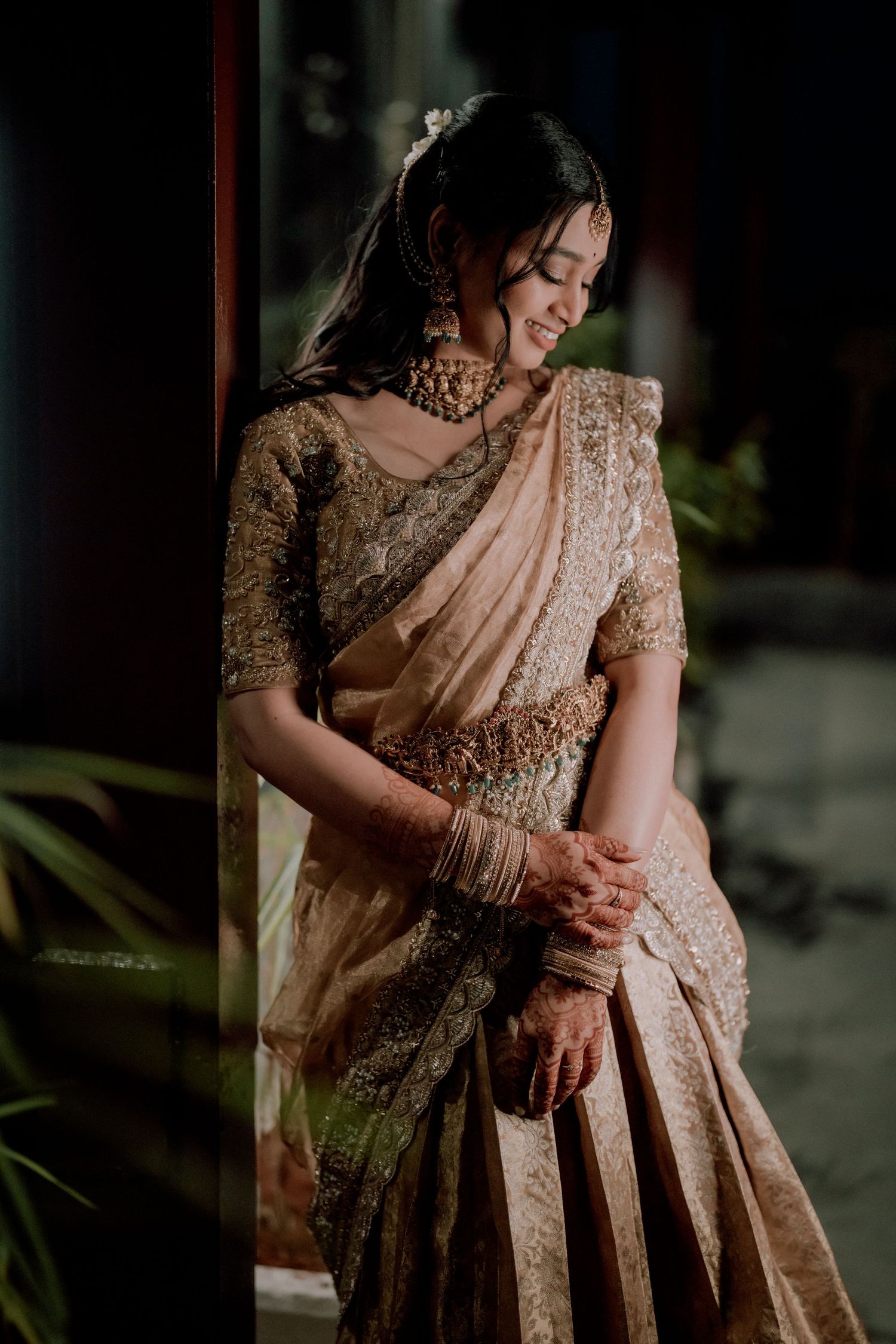 A bride in elegant peach saree and embellished blouse poses gracefully.