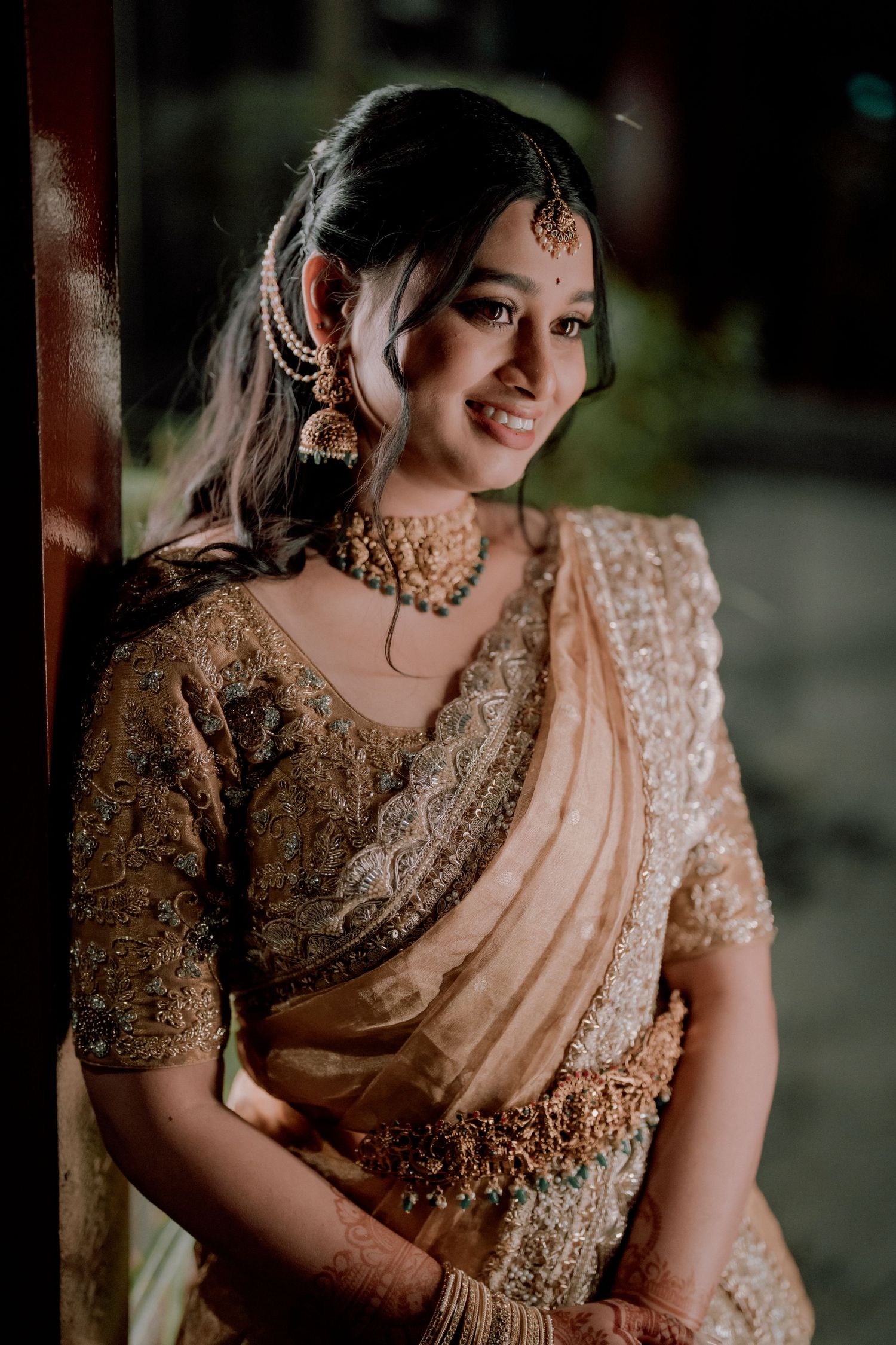 Traditional Indian bride in peach saree and jewelry smiles warmly.