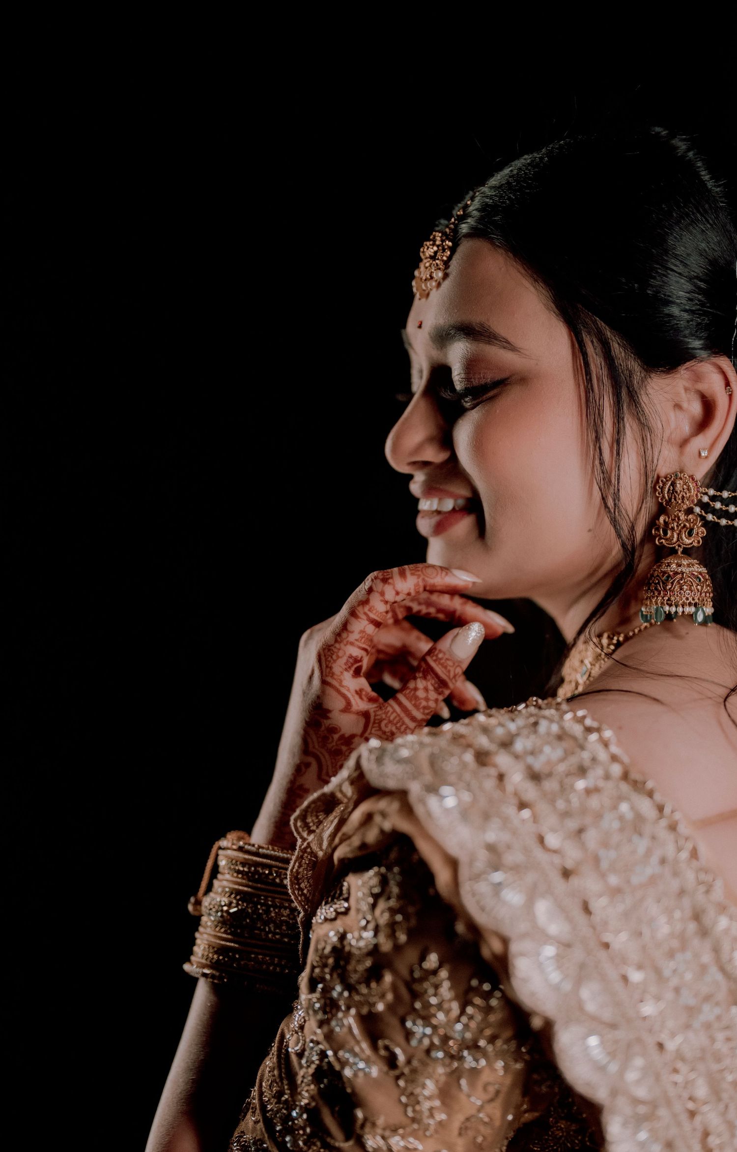 Side profile of bride with mehndi hands and traditional bridal jewelry.