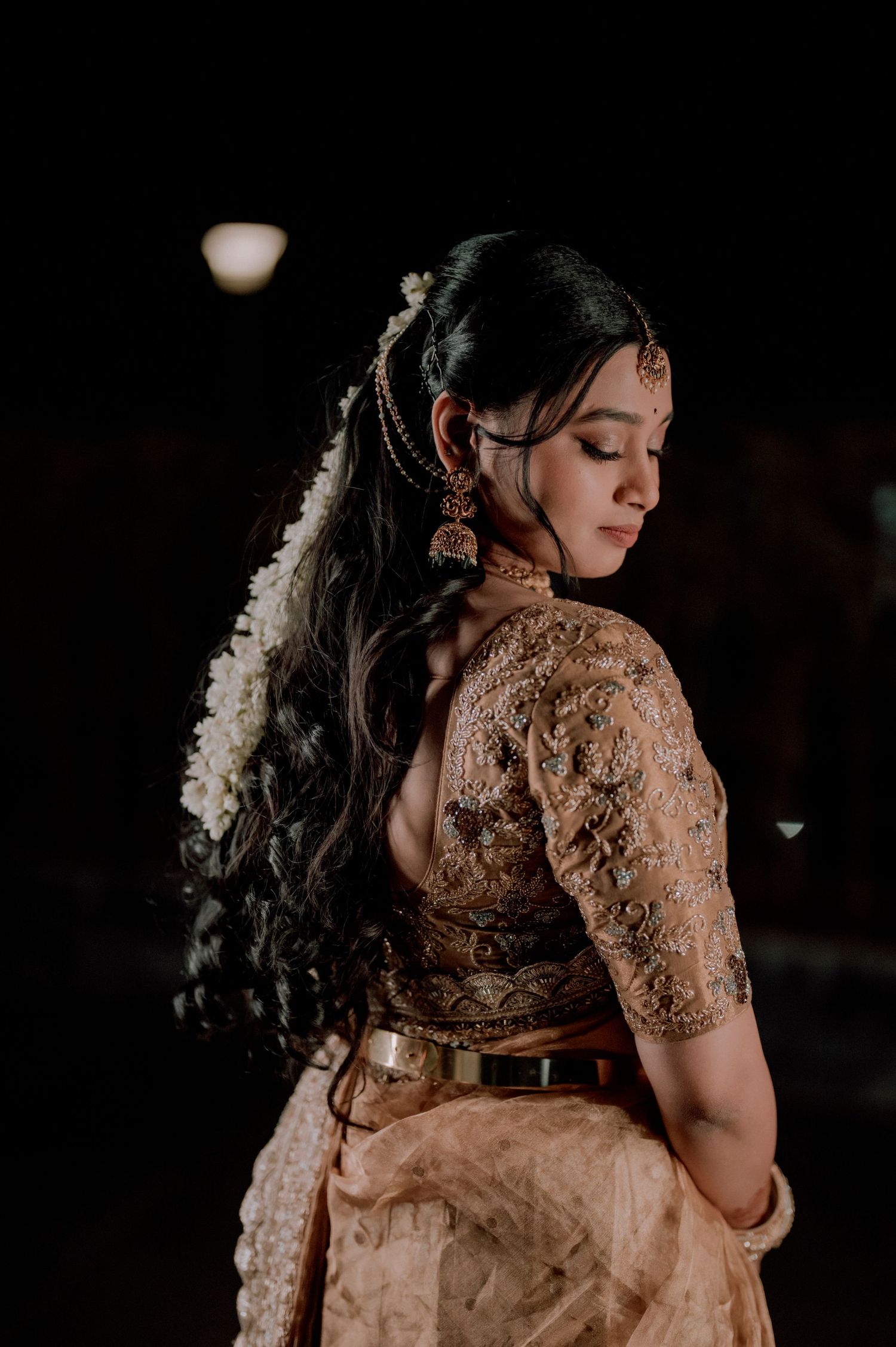 Artistic shot of a bride in beige embroidered attire with traditional jasmine flowers in her hair.