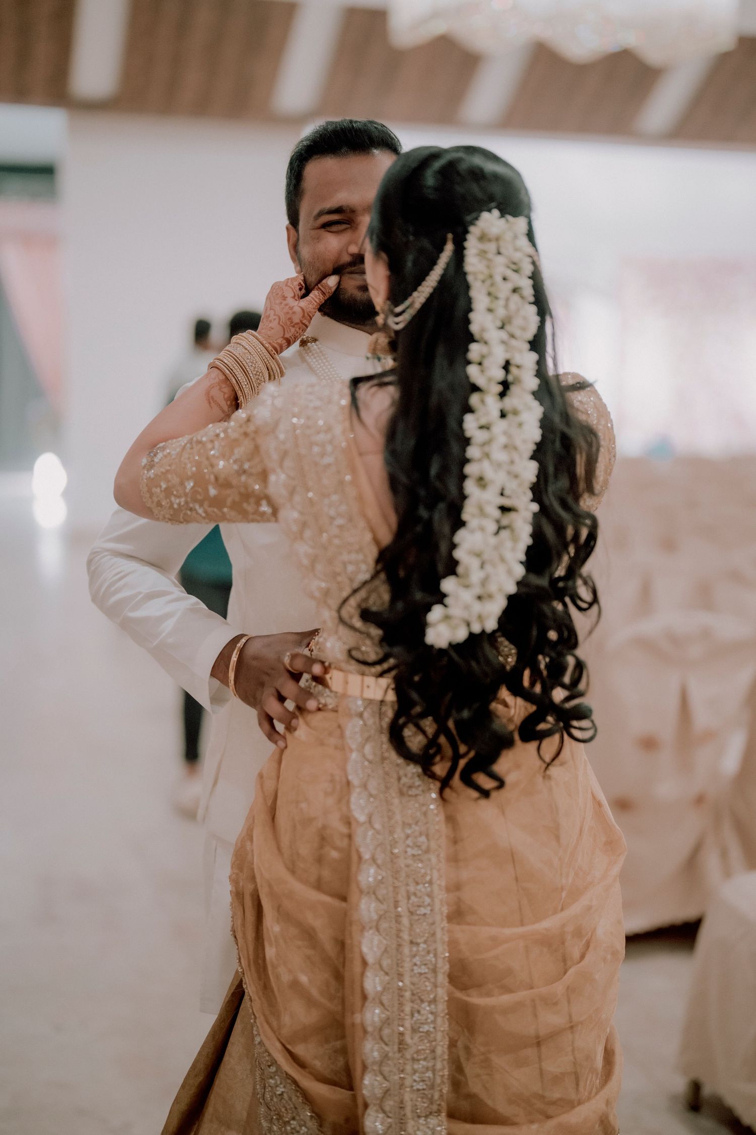 A romantic moment captured during an Indian wedding celebration with traditional floral hair decorations and attire.