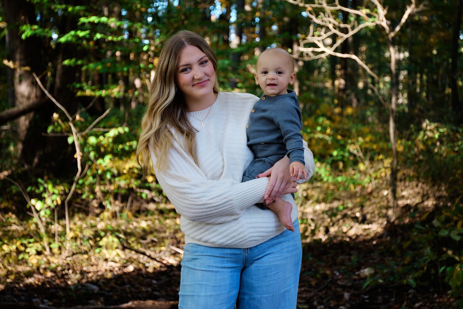A sweet outdoor family portrait of parent and child standing together in a wooded setting.