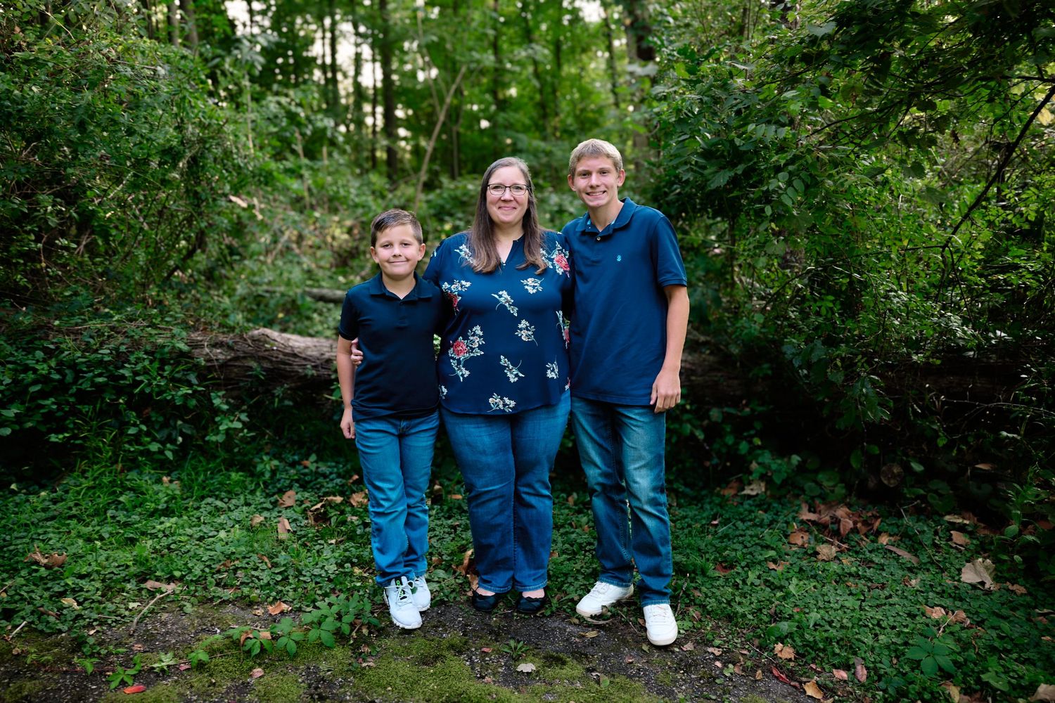 A small group wearing coordinating navy blue outfits poses together in a wooded setting.
