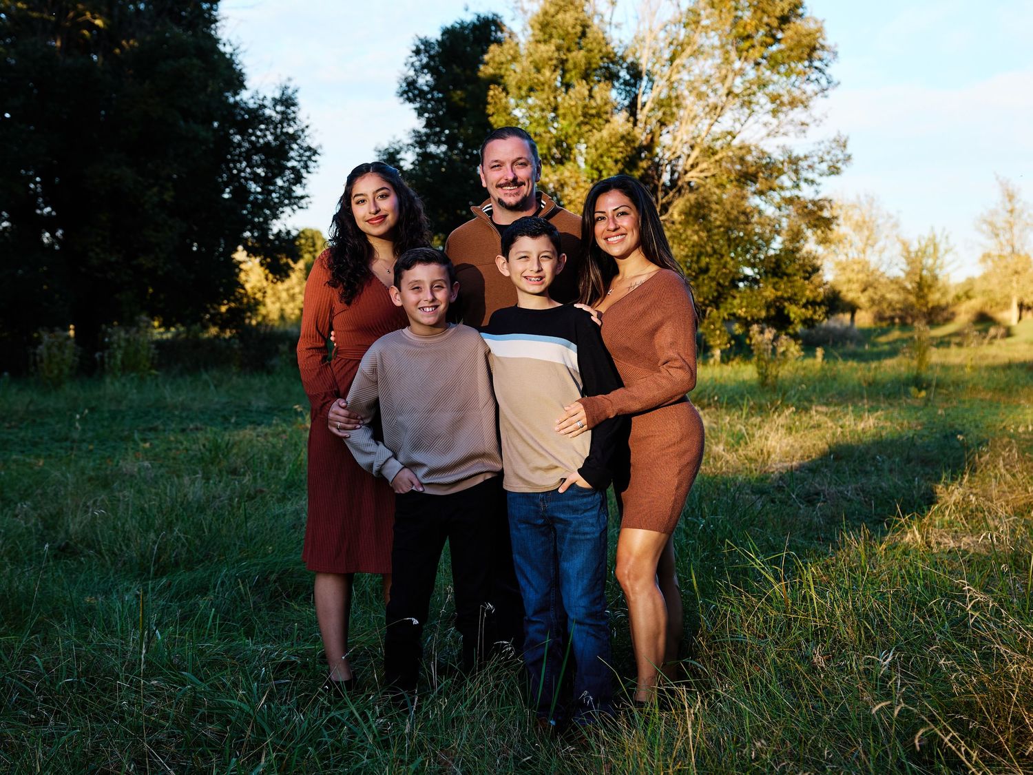 A group stands together in a sunlit grassy field during golden hour as warm sunlight filters through autumn trees.