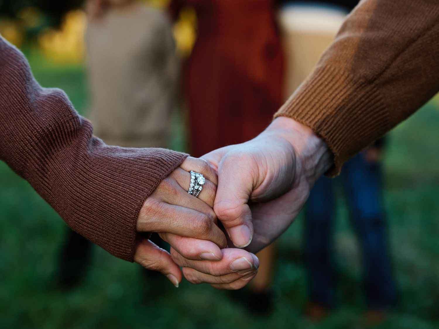A series of hands holding hands in sequence creates a connected chain against a blurred outdoor background.