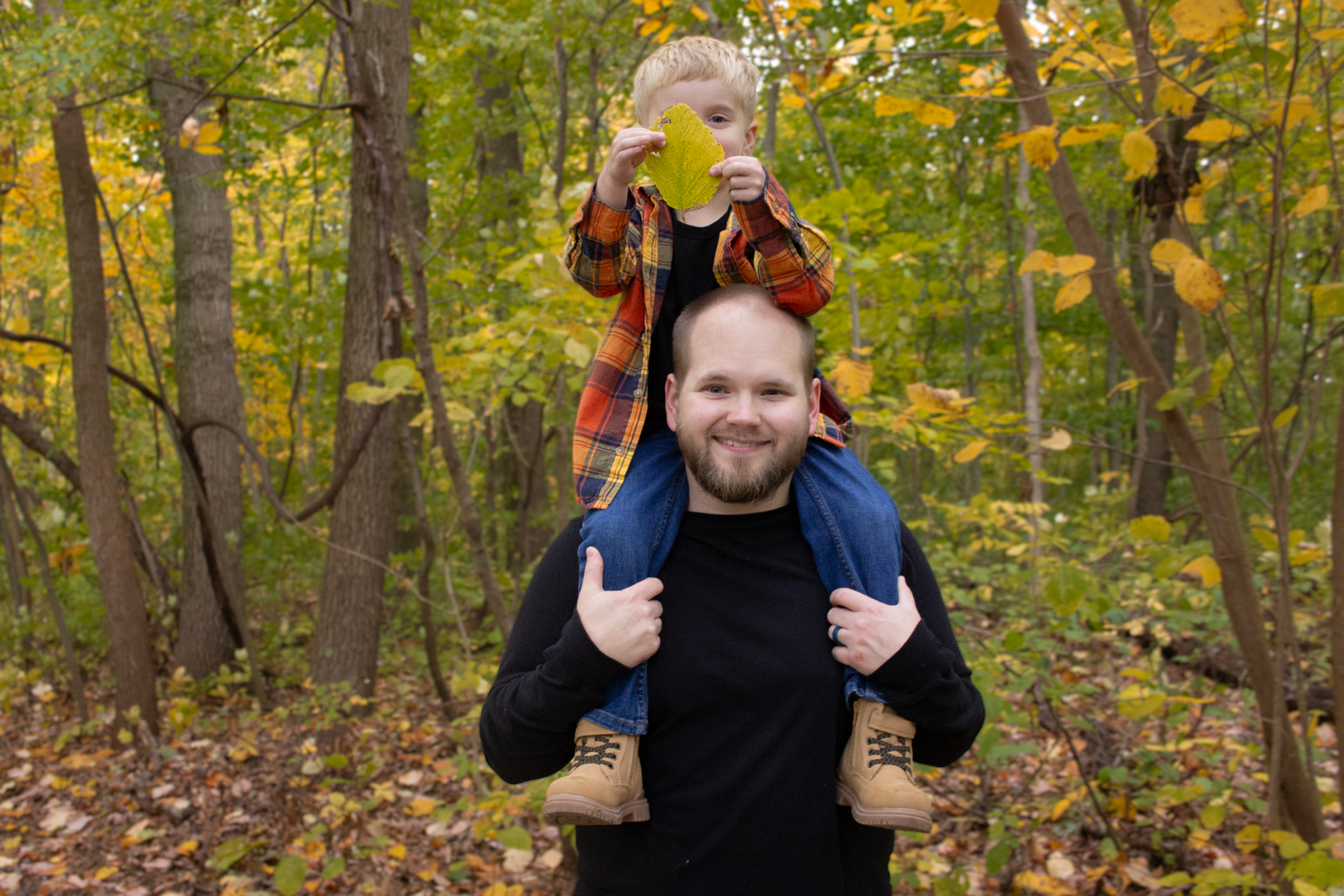 Parent and child enjoying a playful moment in a fall forest setting.
