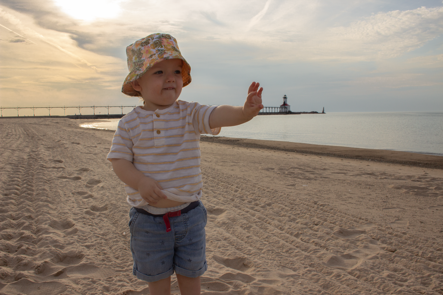 Small child in summer clothes gesturing on a beach at sunset.